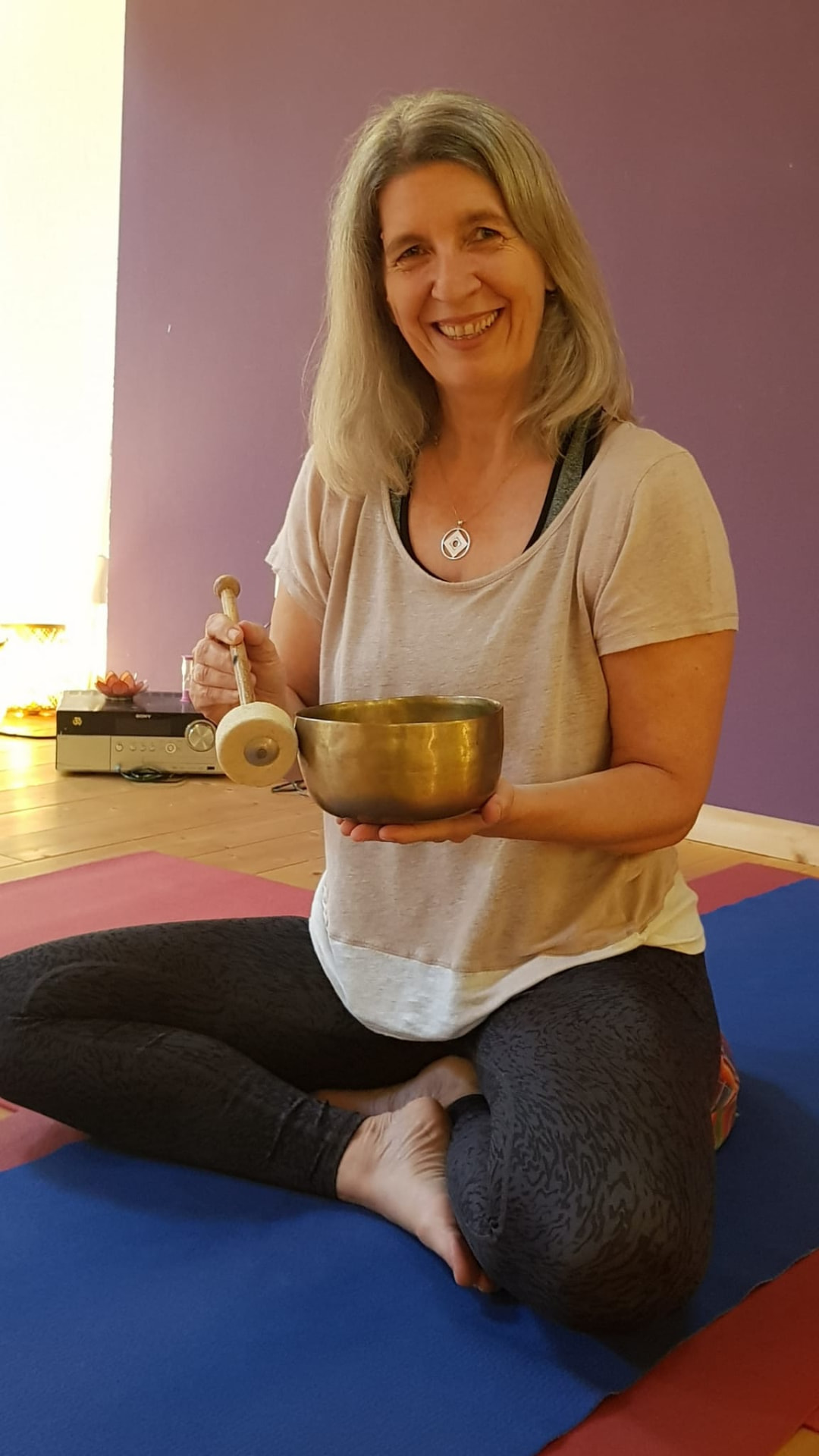 Sabine Langner sitzt auf der Yogamatte und hält eine Klangschale